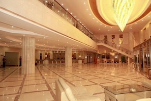A spacious lobby with a high ceiling, a central staircase, and a large chandelier.