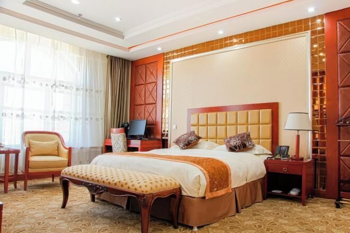 A hotel room with a large bed, a wooden bench, a desk, and a chair.