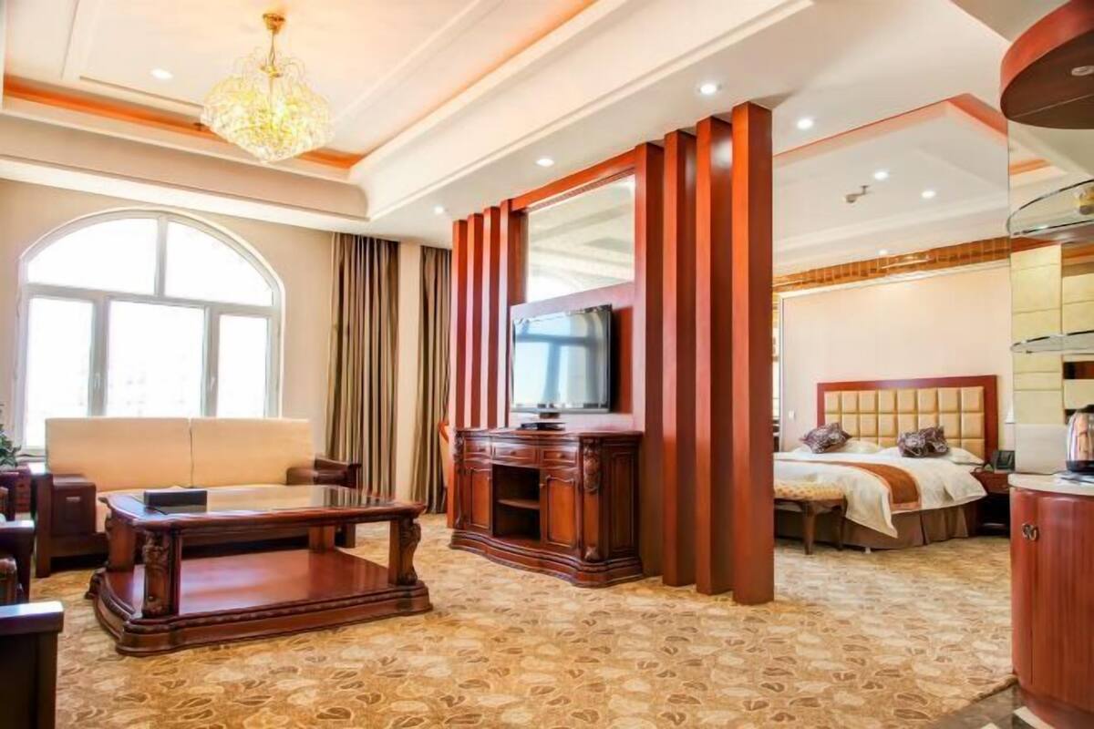 A hotel room with a large window, a sofa, a wooden coffee table, a TV, and a bed with a headboard.