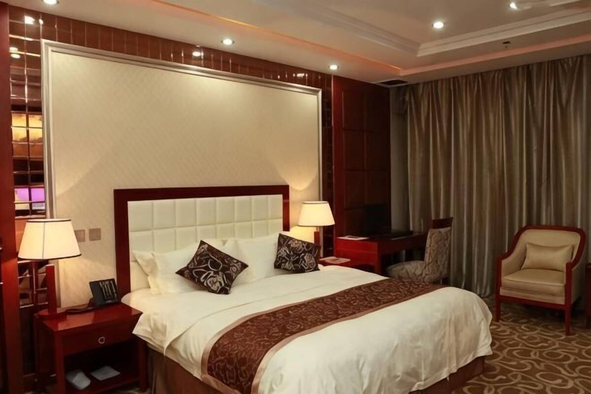 A hotel room with a large bed, two bedside tables with lamps, a TV, a chair, and a curtain.