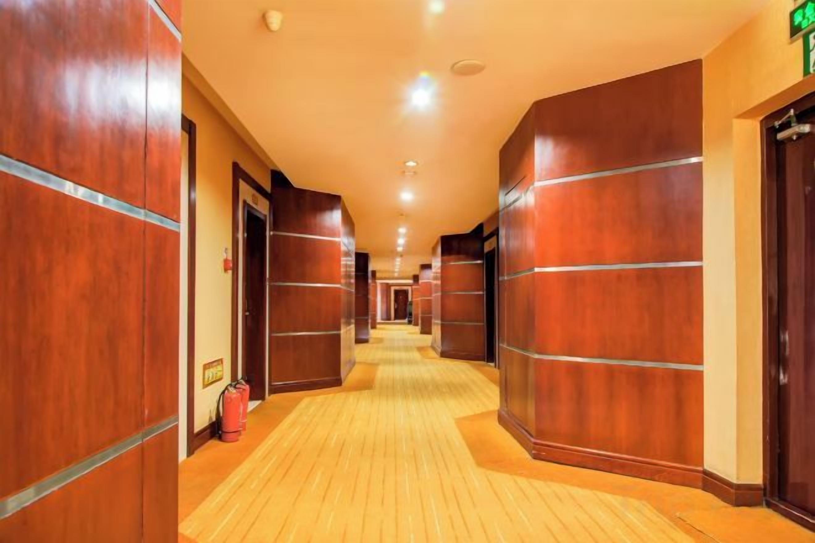 A hotel corridor with wooden walls and doors, a fire extinguisher, and a green exit sign.