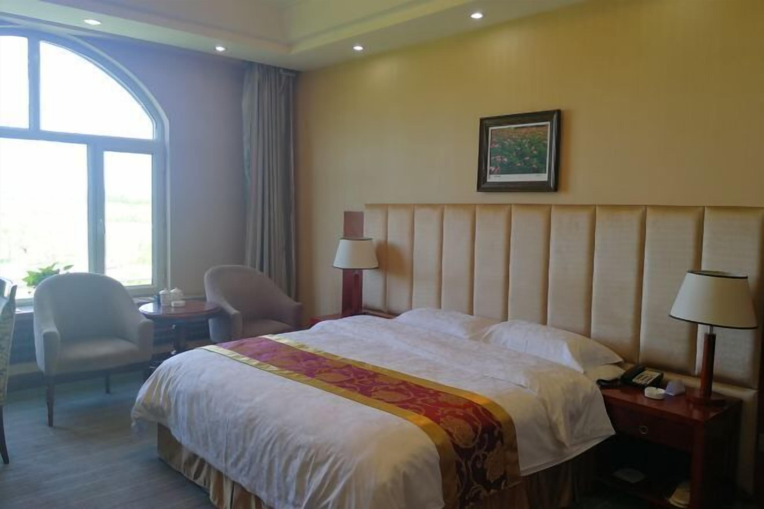 Una habitación de hotel con una cama grande, dos lámparas de noche, una silla, un escritorio y una ventana con cortinas.