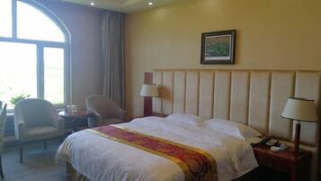 Una habitación de hotel con una cama grande, dos lámparas de noche, una silla, un escritorio y una ventana con cortinas.