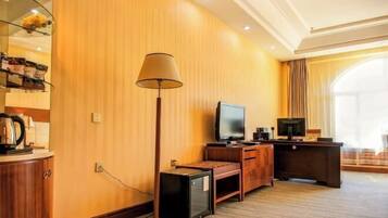 A hotel room with a wooden wall, a flat-screen TV, a desk, a lamp, and a window with curtains.
