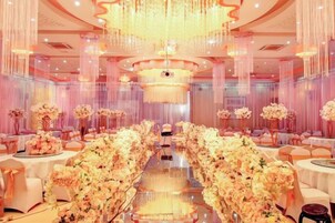 Un salón de banquetes con una larga mesa decorada con flores, candelabros y cortinas colgantes.