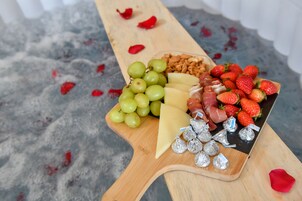 A wooden board with grapes, cheese, strawberries, and wrapped chocolates.