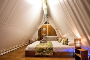 A cozy tented accommodation with a bed, a wooden bench, a hanging light fixture, and a small sink.