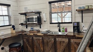 Une cuisine avec des meubles de rangement en bois, un four à micro-ondes, une machine à café et une fenêtre avec des stores.