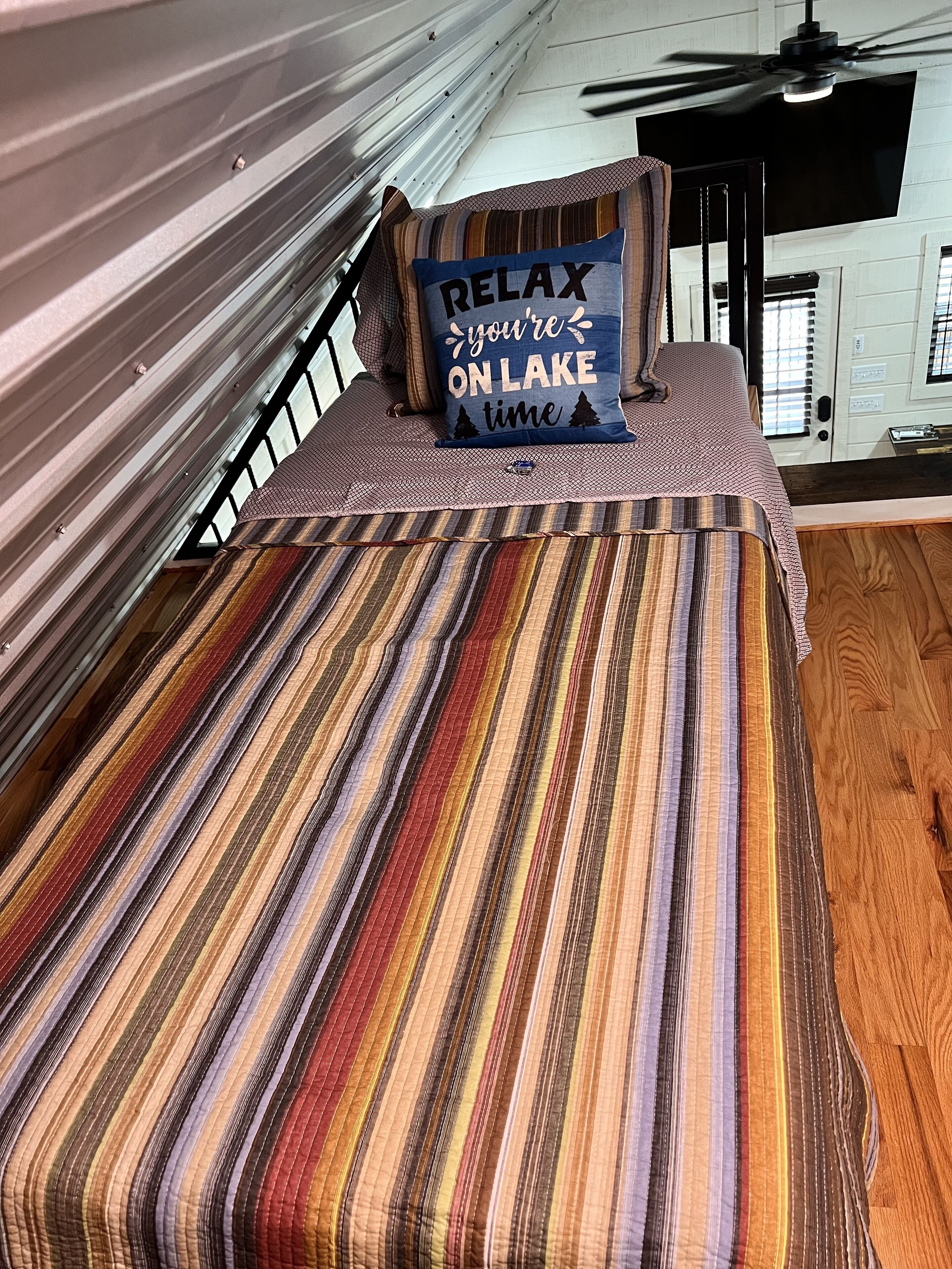 A bed with a striped blanket and a pillow with the text "RELAX you're ON LAKE time".