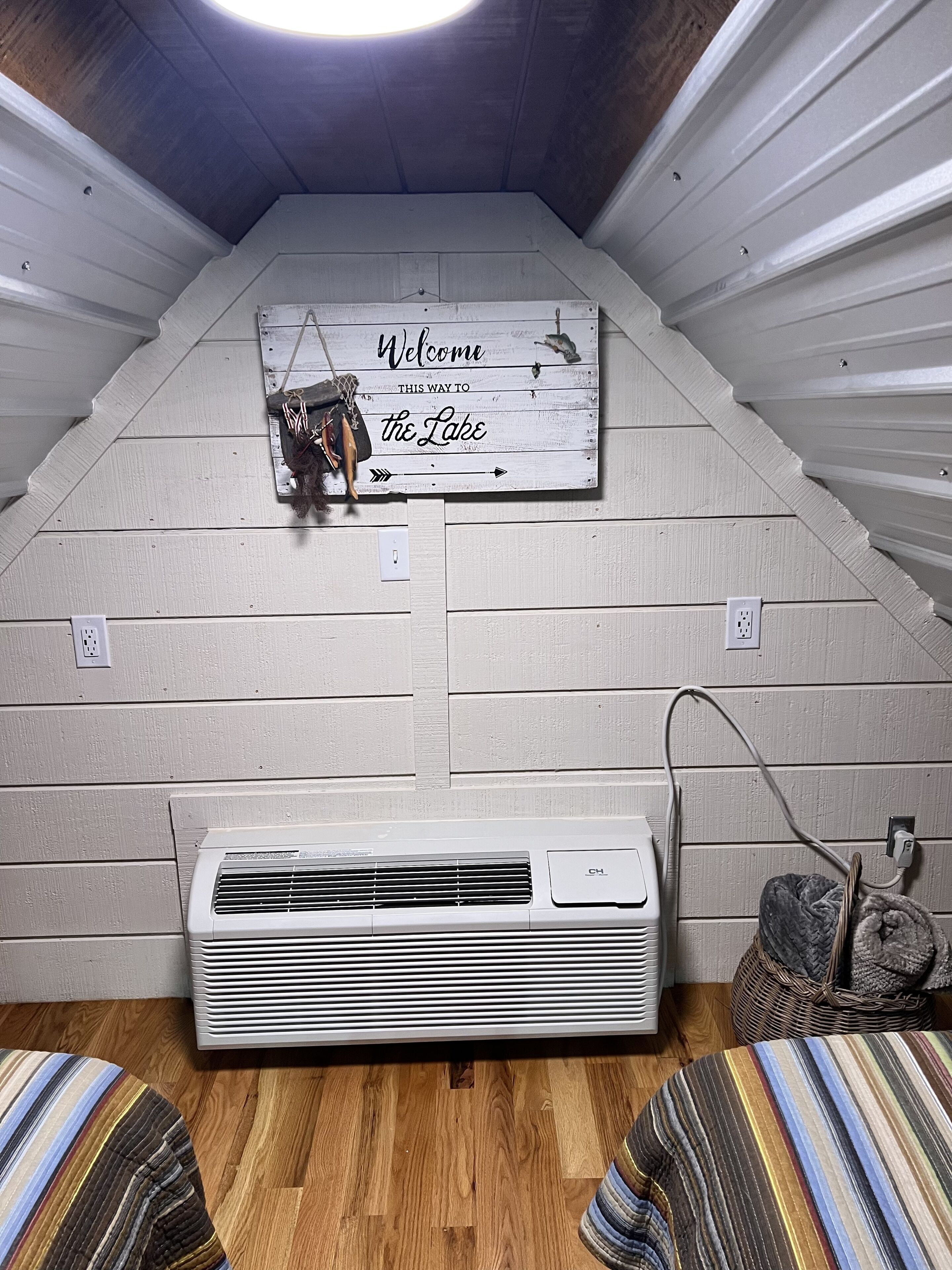 A room with a sloped ceiling, a sign reading "Welcome, this way to the Lake," and an air conditioning unit.