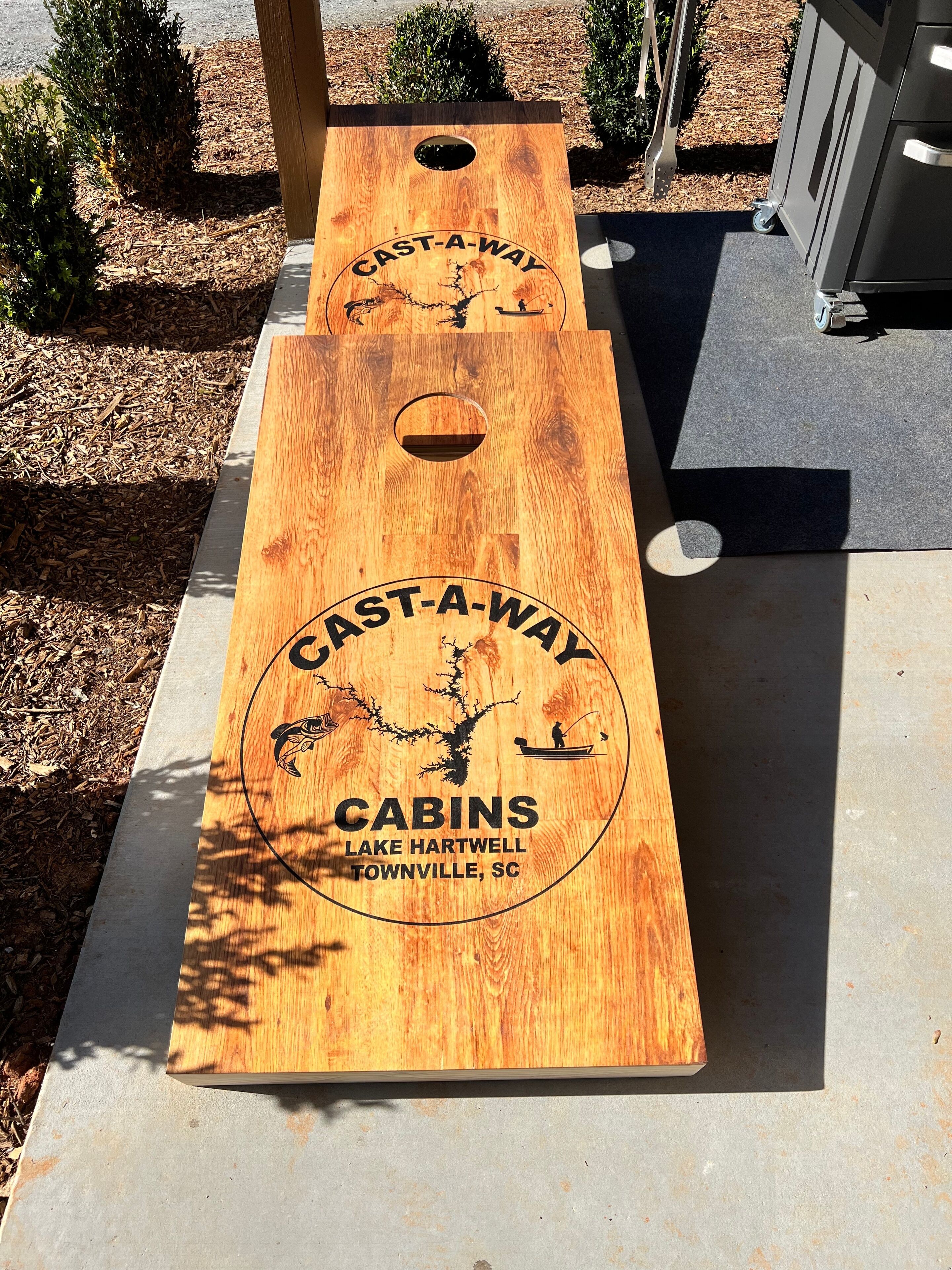Two wooden shuffleboard tables with 'CAST-A-WAY CABINS LAKE HARTWELL TOWNVILLE, SC' engraved on them.