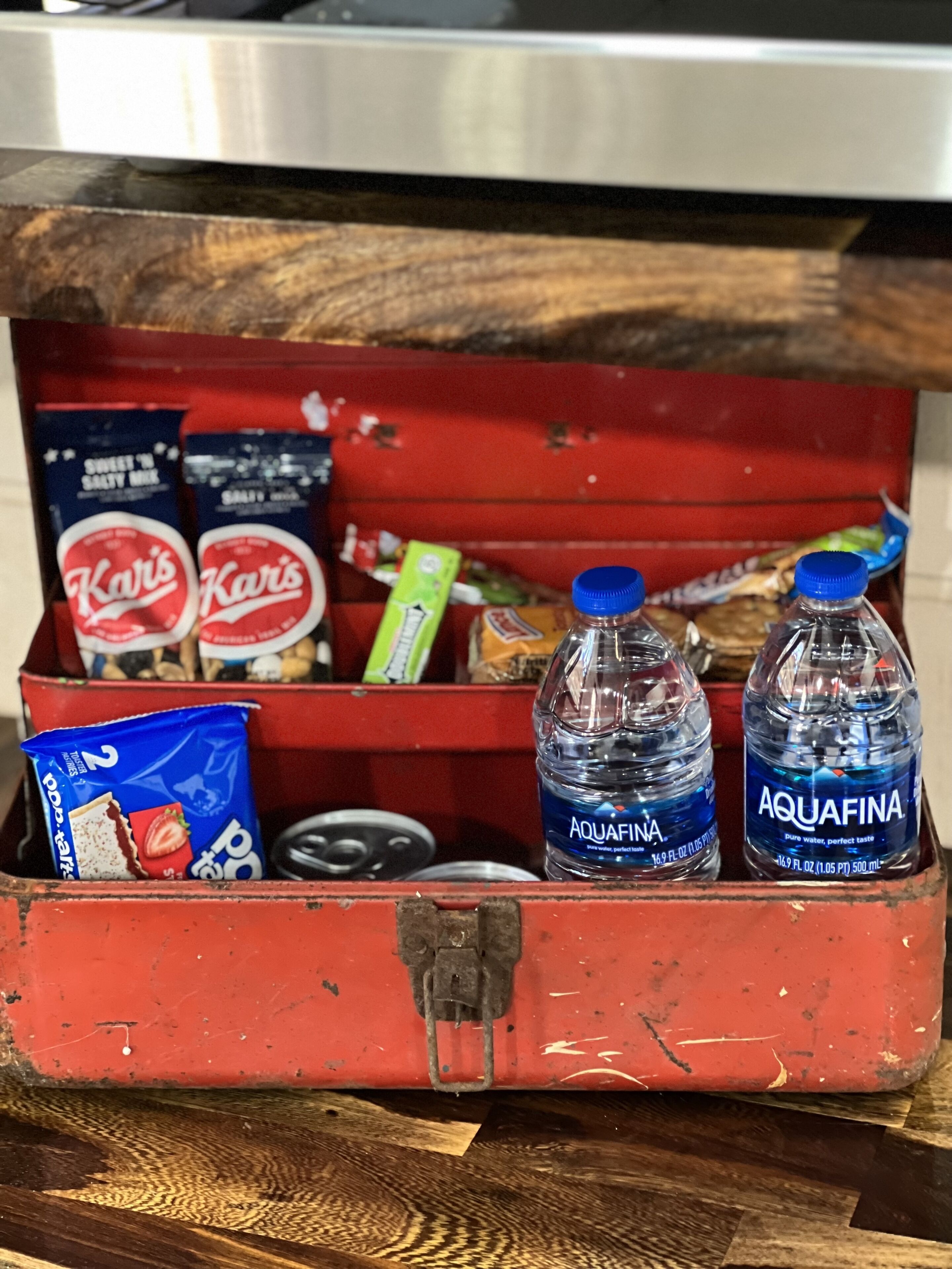 A red toolbox containing snacks, two bottles of Aquafina water, and a packet of pop tarts.