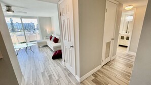 Un appartamento moderno con una zona giorno che include un divano e un tavolino in vetro, un corridoio con una porta e vista su un balcone.
