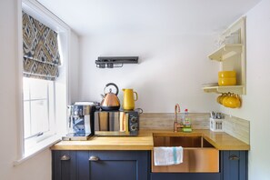 Una cocina con cafetera espresso integrada, hervidor y lavamanos.