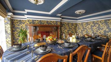 Un comedor formal con papel tapiz azul y dorado, sillas de madera y una mesa dispuesta para una comida.