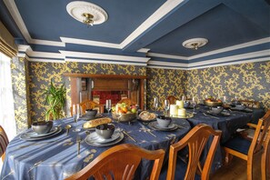 Un comedor formal con papel tapiz azul y dorado, sillas de madera y una mesa dispuesta para una comida.