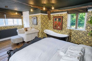 A bedroom with a large bed, a chair, a vintage-style sink, and patterned wallpaper.