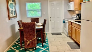 A compact kitchen with a dining area, featuring a small table and chairs, a window, and a refrigerator.