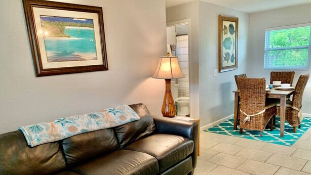 A living room with a leather sofa, a dining table with wicker chairs, a lamp, and a patterned rug.