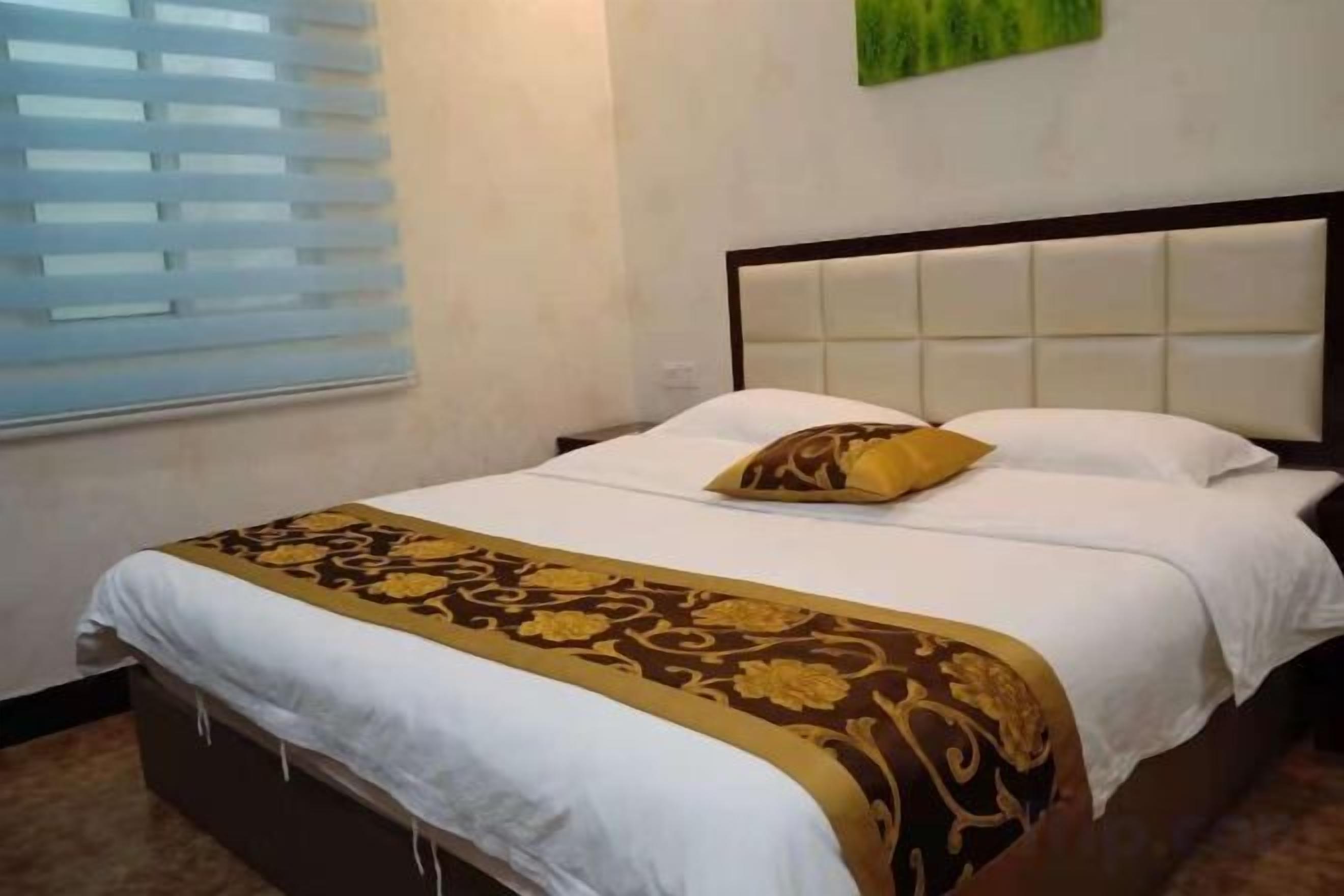 Un letto rifatto con una testiera, una finestra con persiane e un addobbo murale verde.