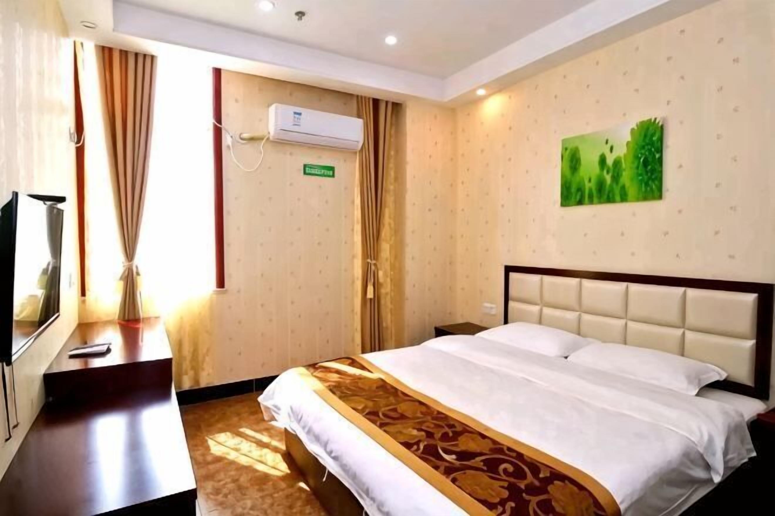 A hotel room with a bed, a desk, a television, and an air conditioning unit.