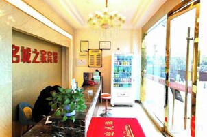 A hotel reception area with a marble counter, a red carpet, a vending machine, and a view of the outside through a glass door.