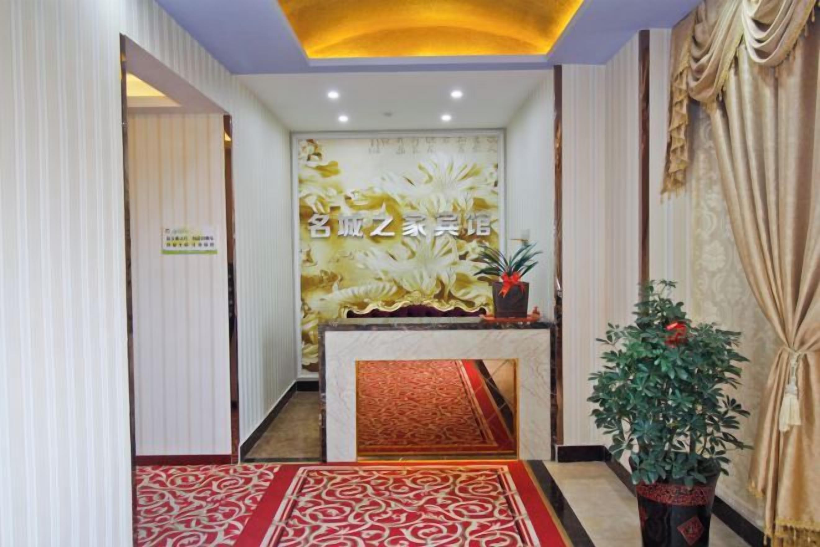A reception area with a decorative wall, a reception desk, a red patterned carpet, and a potted plant.