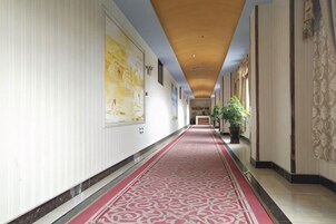 A hotel corridor with a patterned carpet, a reception desk, and a potted plant.