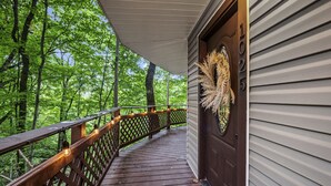Une terrasse en bois avec une rambarde, une porte décorée d’une guirlande et une vue sur une forêt.