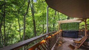 Une terrasse en bois avec un jacuzzi, des chaises longues et une pergola recouverte de verdure.