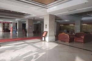 A spacious lobby with a red carpet, a reception desk, and leather seating.