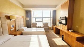 A hotel room with two beds, a TV, a desk, and a window with a city view.