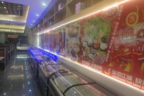 Un couloir avec un escalier mécanique, une longue table éclairée de lumière bleue et un mur orné de publicités pour des produits alimentaires.