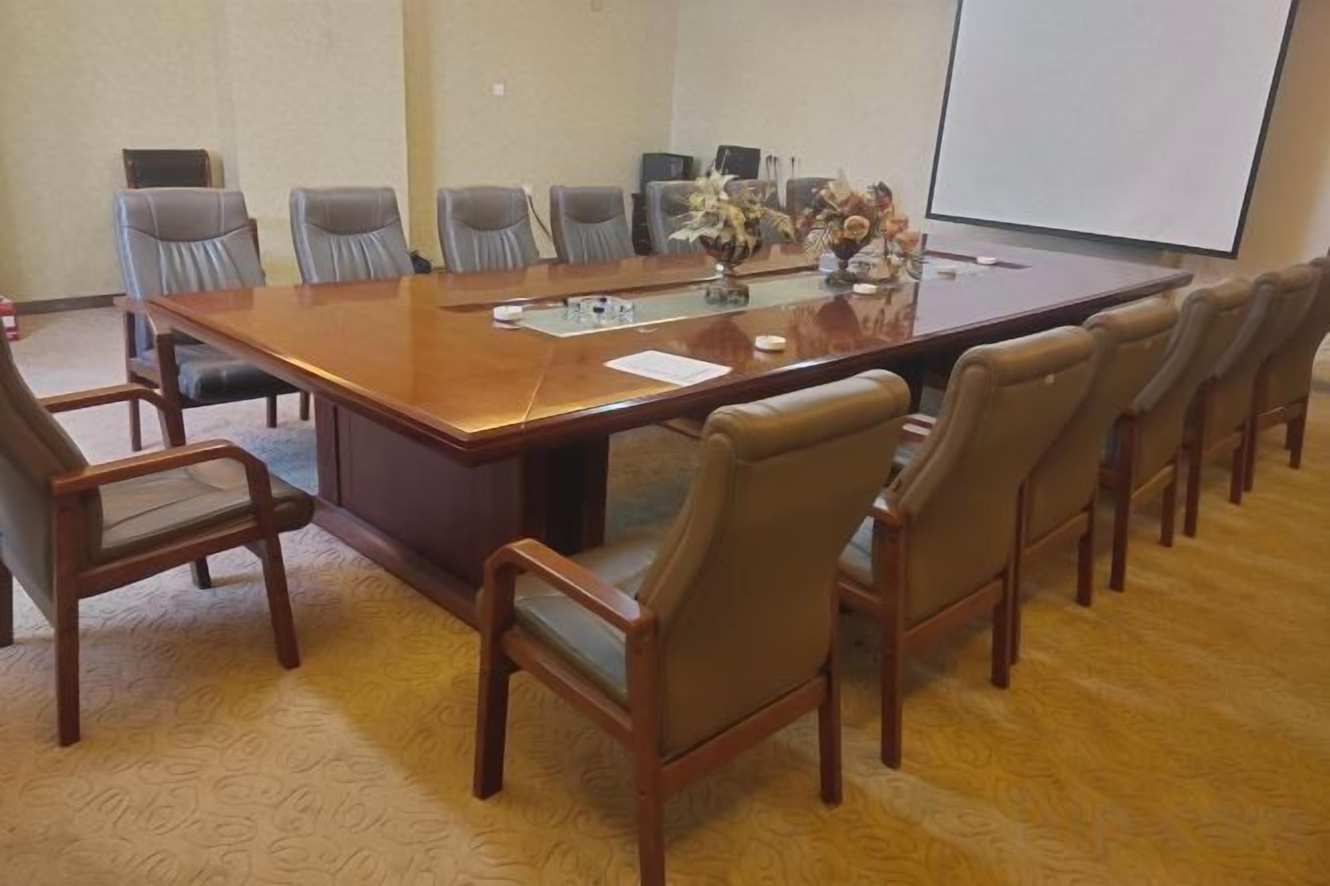 A conference room with a large rectangular table, multiple chairs, and a projector screen.
