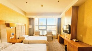A hotel room with two beds, a TV, a desk, and a view of the city. - Jiaxing Hotel (Ordos)