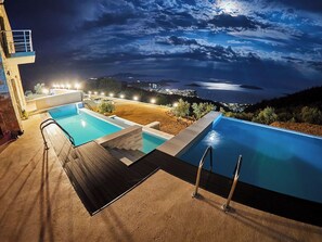 Une piscine avec une terrasse en bois et une vue sur la ville la nuit.