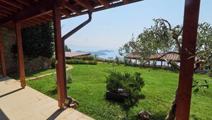 Une pergola en bois, dotée d’un sol en pierre, d’une pelouse bien entretenue et offrant une vue sur la mer et les montagnes en arrière-plan.