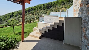 Un escalier extérieur moderne menant à un espace piscine, avec vue sur une colline verdoyante.