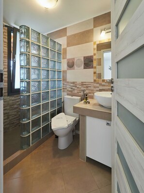 A modern bathroom with a glass partition, a toilet, a sink, and a mirror. - Villa Denise Exclusive (Sporades)