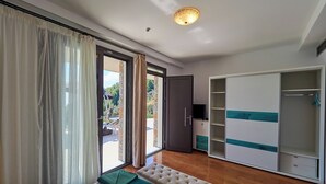 Un dormitorio con cama, un banco, un armario y vistas a través de un ventanal.