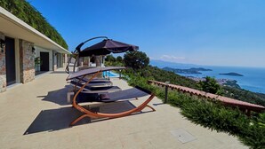 Una terraza con tumbonas y piscina, con vistas a un paisaje costero.