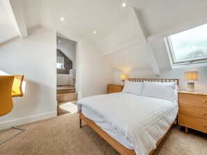 Une chambre à coucher comprenant un lit, des tables de chevet, une fenêtre et un escalier menant à un étage supérieur.