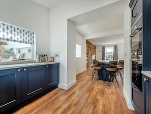 A modern kitchen with dark blue cabinets, a wooden floor, and a dining area with bar stools.