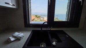 A kitchen with a black sink, a window with a view of a coastal town, and a towel on the counter. - Villa Noa Exclusive 4 Bedrooms (Skiathos)