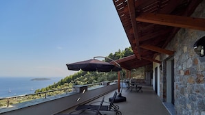 A covered outdoor area with a view of the sea, a stone wall, and a seating area with a table and chairs. - Villa Noa Exclusive 4 Bedrooms (Skiathos)