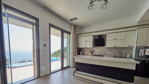 A modern kitchen with a large island, sliding glass doors leading to a pool, and a view of the ocean. - Villa Linda (Skiathos)