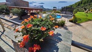 A stone ledge with orange flowers, a pool, and a view of the sea and islands. - Villa Linda (Skiathos)