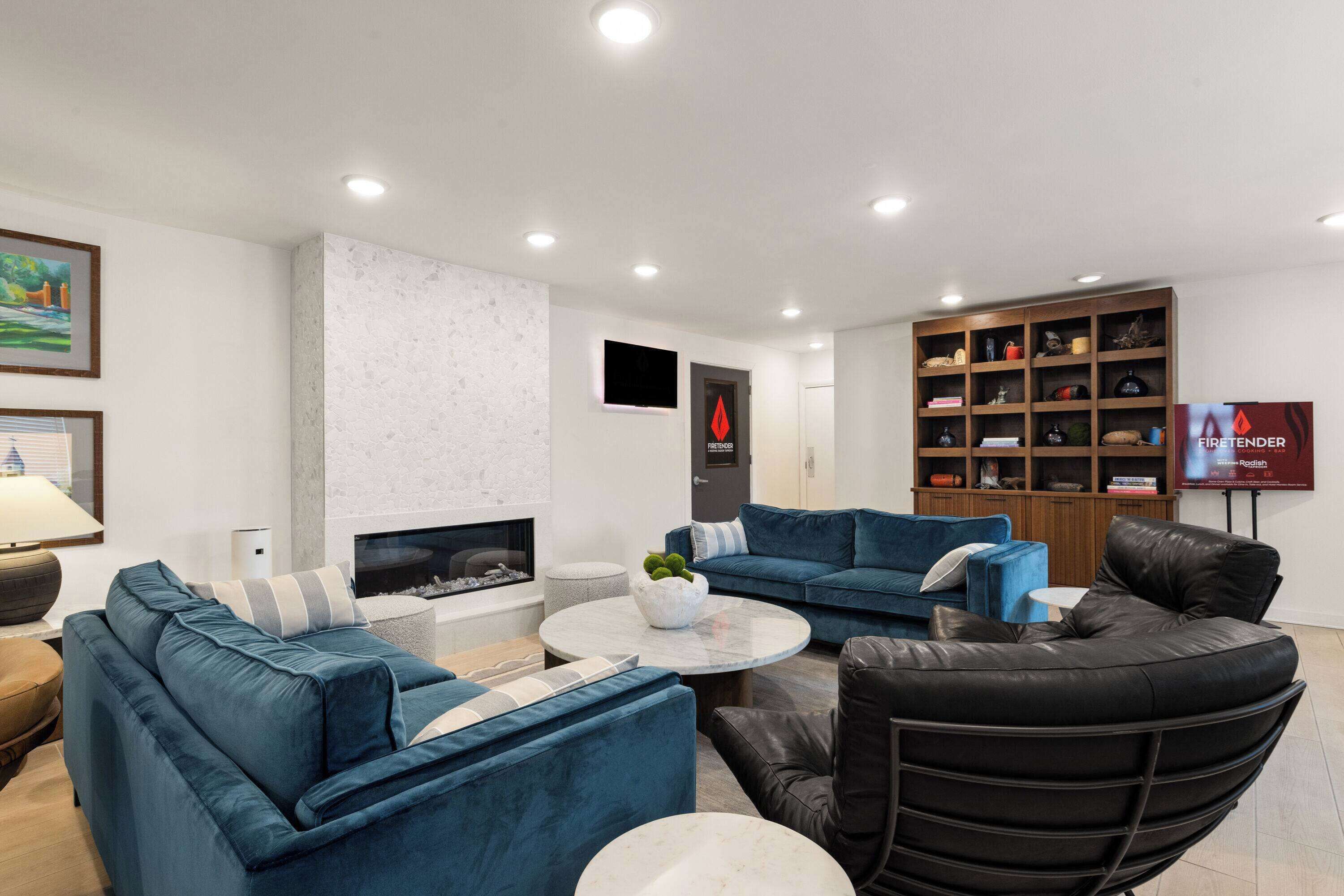 Una sala de estar moderna con chimenea, sofás azules, un sillón de cuero negro y una estantería.
