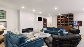Una sala de estar moderna con chimenea, sofás azules, un sillón de cuero negro y una estantería.