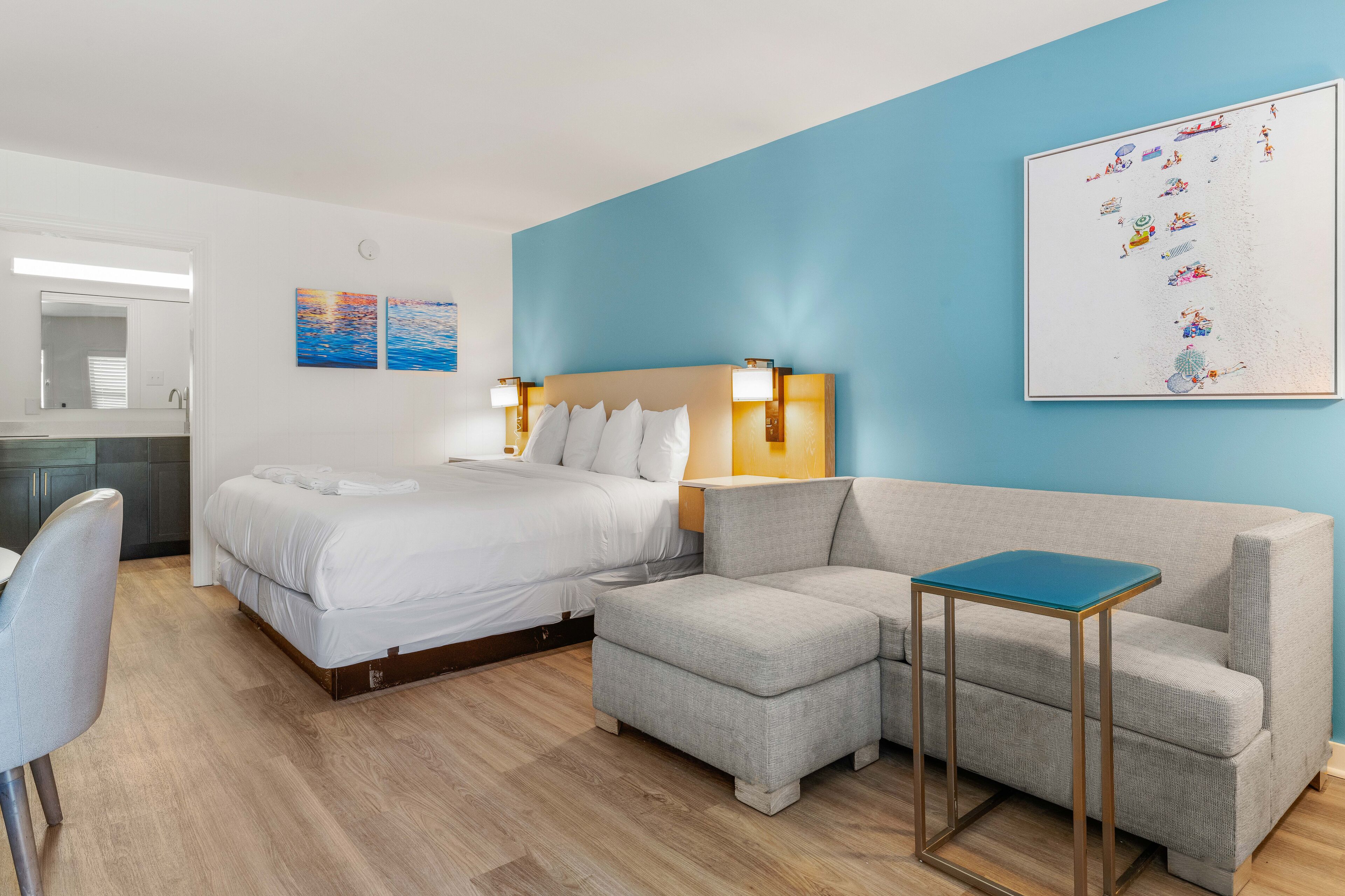 Una habitación de hotel con una cama, un sofá gris, una mesita y una pared decorada con obras de arte.